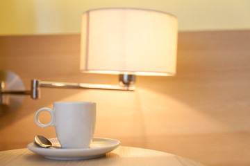 cup of coffee on wooden table at the hotel with a lamp in the ba