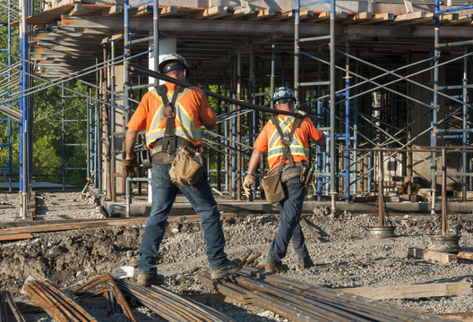 Two construction workers carrying metal rods on their shoulder