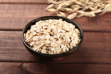 Oat stems and oat flakes in ceramic bowl on wooden table