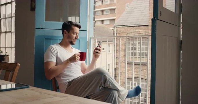 Morning coffee for happy man using smart phone at home in pajamas