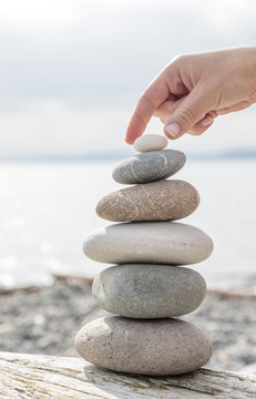 Close-up of woman's hand balancing a stack of stones on a sunny beach