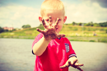 Child playing outdoor showing dirty muddy hands.