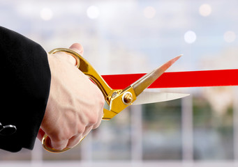 Businessman cutting red ribbon with pair of scissors close up