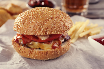 Big tasty hamburger with snacks and glass mug of light beer on wooden table