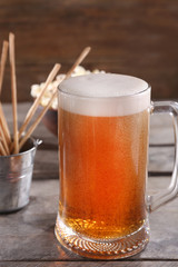 Glass mug of light beer with snacks on wooden table, close up