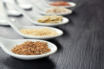 Different kinds of seeds in spoons on wooden table