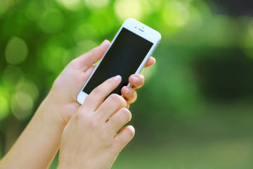 Female hands holding a mobile phone outdoors, on blurred background