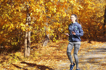 Fototapeta premium Young beautiful woman running in autumn park and listening to music with headphones.