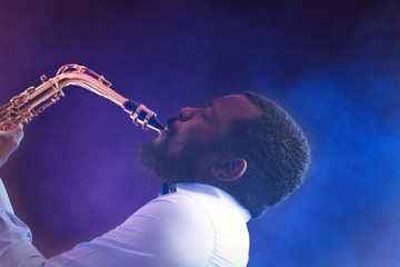 African American jazz musician playing the saxophone against colorful smoky background