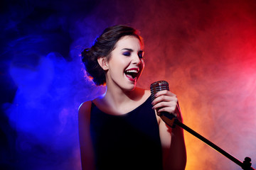 Young beautiful woman singing in colourful smoke, close up