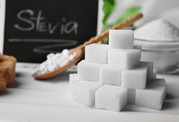 Pile of sugar cubes and stevia on white wooden background