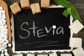 Word STEVIA written on black board and sugar on wooden background