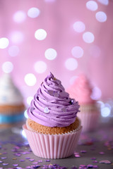 Cupcake with purple cream icing on a glitter background, close up