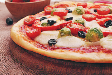 Delicious pizza with cheese and vegetables on wooden cutting board closeup