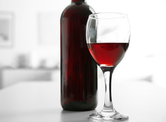 Glass of red wine with bottle on blurred interior background