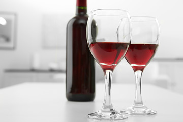 Glasses of red wine with bottle on blurred interior background