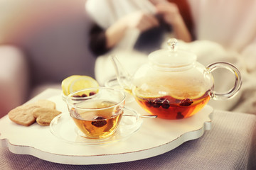 Tea cup and kettle on white wooden mat beside sofa on the knitting woman background