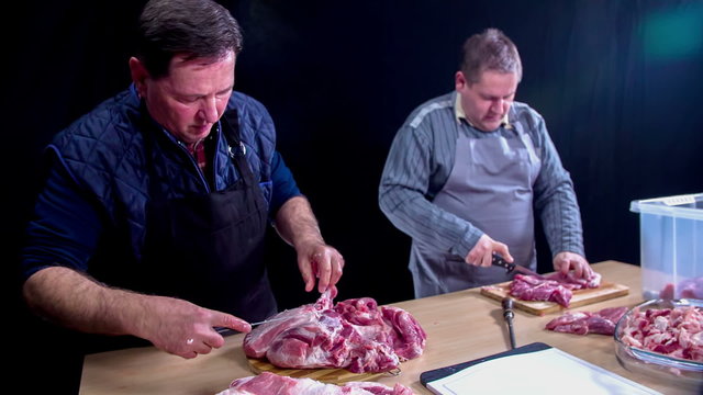 Two men are deeply concentrated in cutting large amounts of meat