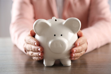 Woman holding in hands piggy bank at the table