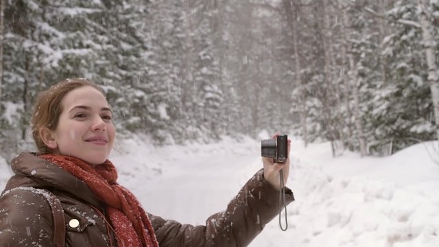 Girl taking a selfie under the snow in a winter forest