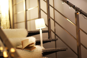 Resting-place with electric garland, book and lamps on modern stairs