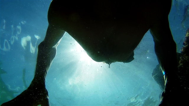 An underwater shot of a swimming man against bright sunshine.Slow motion video.