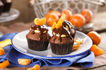 Three tasty cupcakes with slice of mandarin and chocolate on a plate over wooden background