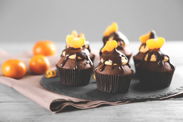 Tasty cupcakes with slice of mandarin and chocolate on slate plate over light wooden background