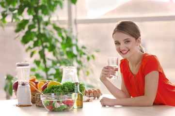 Young woman drinking water near table with fruits and vegetables in the kitchen