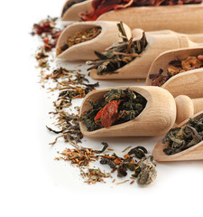 Variety of dry tea in wooden scoops isolated on white, copy space