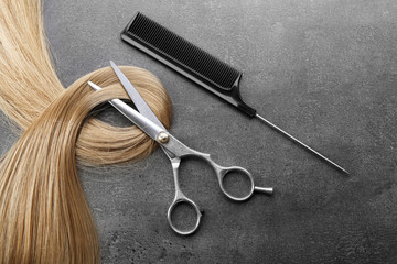 Hairdresser's scissors with comb and strand of blonde hair on grey background