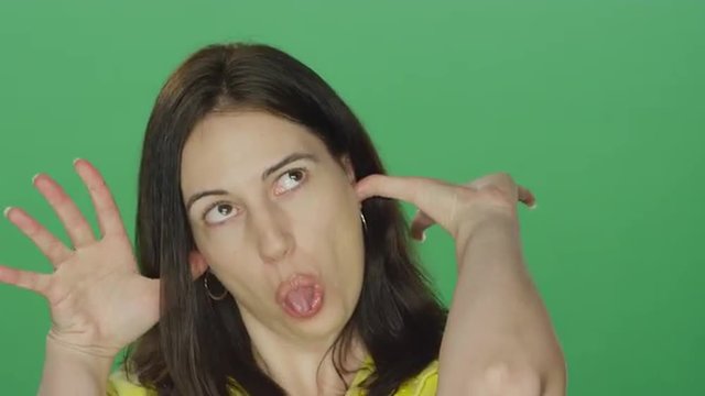 Young brunette woman smiling and making silly faces, on a green screen studio background