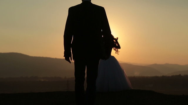Silhouettes of groom coming to his bride on sunset background in mountains