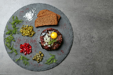 Delicious beef tartare with ingredients on dark background