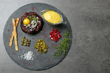 Delicious beef tartare with ingredients on dark background