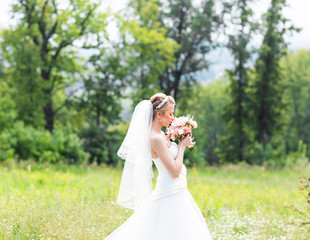 Beautiful bride with wedding bouquet of flowers outdoors in green park.