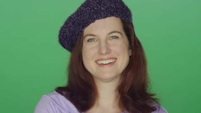 Young redhead woman wearing a beret laughing and smiling, on a green screen studio background