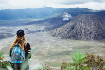young girl in jacket a baseball cap with a backpack, traveling the world, stands on a hill and looks at the volcano, beautiful scenery, new discoveries, emotions, outdoor portrait, close up, turist
