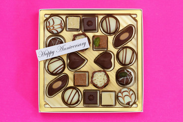 Happy Anniversary card with box of assorted chocolates on pink background
