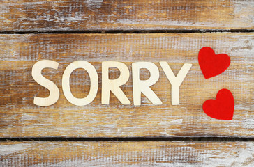 Sorry written with wooden letters and two red hearts on rustic surface
