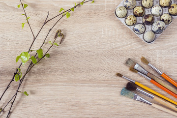 Quail eggs in the tray with paintbrushes and spring twig on a wo