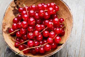 Redcurrant on a branch close to a wooden bowl.
