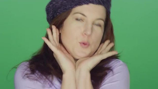 Young redhead woman wearing a beret smiling and making silly faces, on a green screen studio background