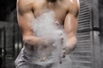 Mid section of shirtless man clapping hands with talc