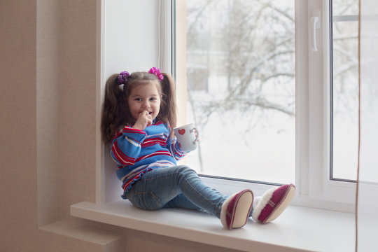 Little beauty girl with cup at the window