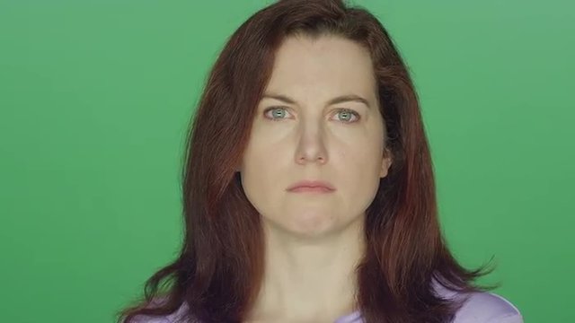 Young redhead woman looking sad, on a green screen studio background 