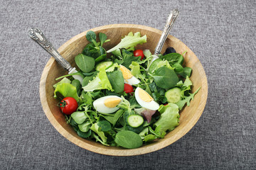 insalata verde con uovo  pomodori e cetrioli in ciotola di legno sfondo grigio