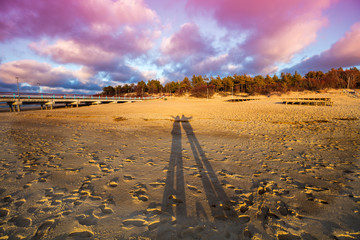 Long shadows of man and woman on the beach at sunset