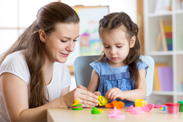 child girl and woman playing colorful clay toy at nursery or kindergarten