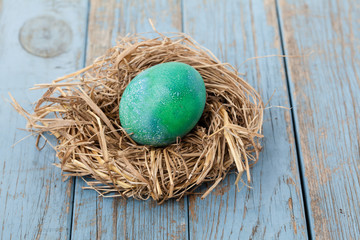 grönmålat ägg i ett fågelbo på sliten blå träbakgrund